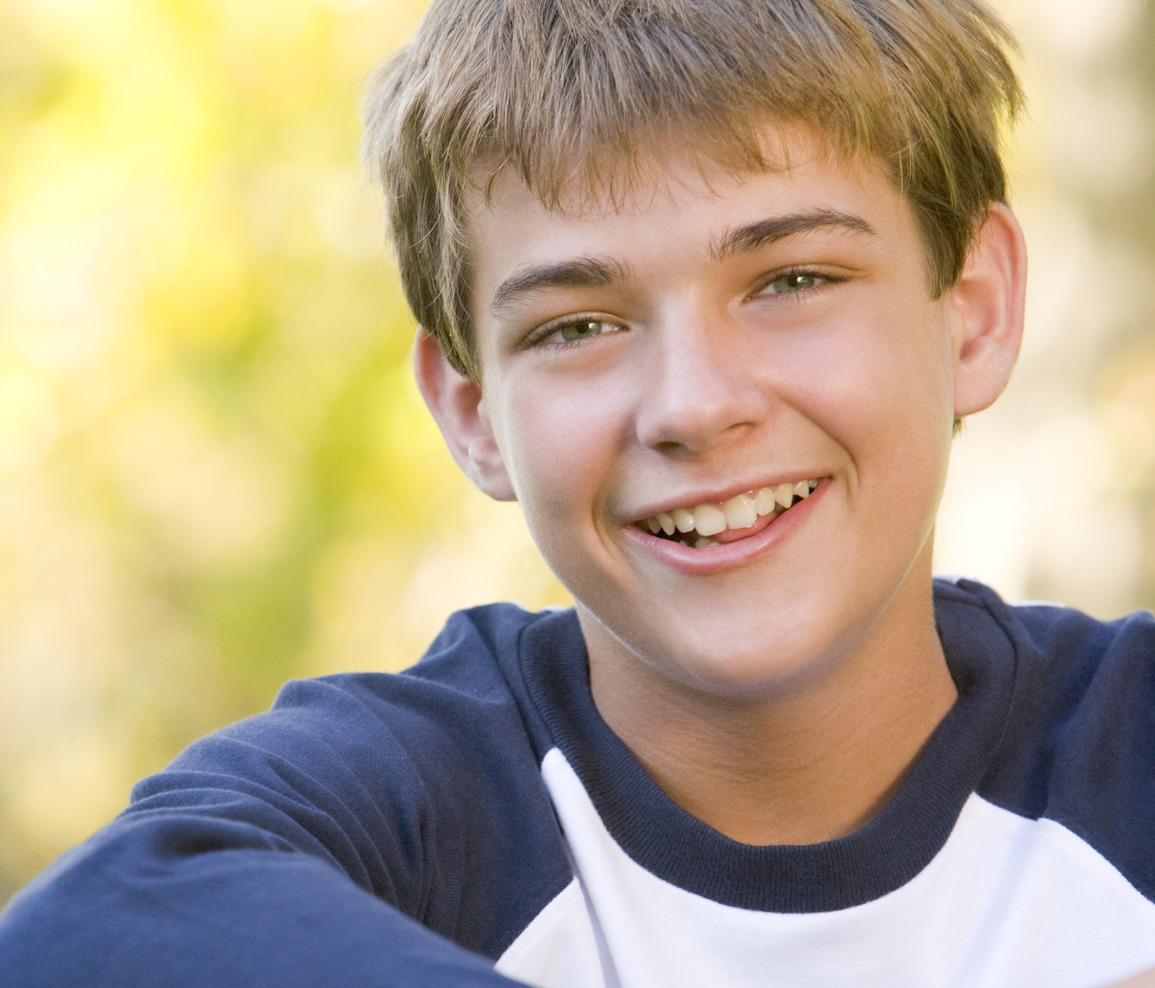 Young boy sitting outdoors smiling. 